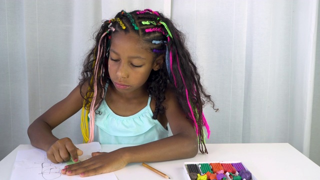 一名牙买加混血女孩，梳着彩色辫子，在停下来沉思后用绿色粉笔给一幅画上色视频下载