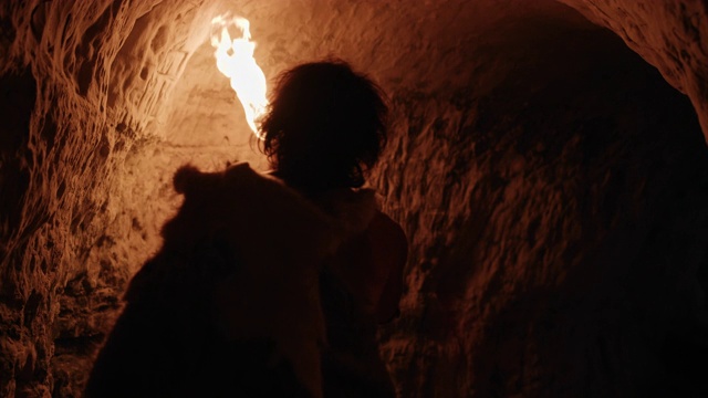 穿着兽皮的原始穴居人在夜晚探索洞穴，手持火把看着墙上的画。尼安德特人寻找安全过夜的地方。后视图后视频素材