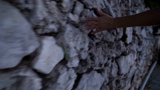 女人的手缓慢地滑过古老的石墙。视频素材