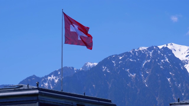 瑞士国旗在阿尔卑斯山脉的背景站在房子的屋顶视频素材