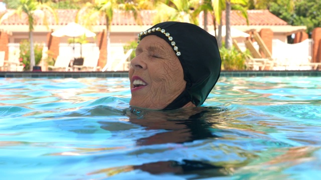 从水面上看，高级花样游泳运动员微笑着在例行训练后挂在泳池里视频素材