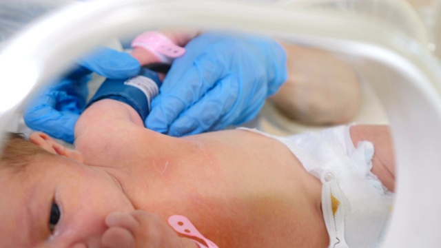 新生儿孵化器，医院强化治疗:CCU, ICU, ITU。戴着蓝手套的医生牵着婴儿的小手。产科诊所的医生监督。4 k视频素材