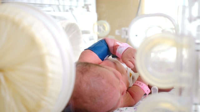 妇产科医院。在医生监护下的保育箱中的早产儿。特写镜头护士的手在蓝色手套触摸新生婴儿的小脚和手。4 k视频素材