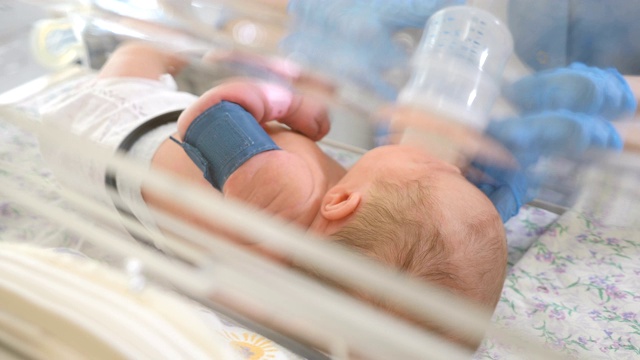 产科诊所。拯救生命的概念。在医生监护下的保育箱中的早产儿。特写镜头，护士的手在蓝色手套拿着奶瓶。4 k视频素材