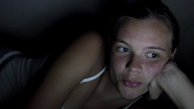 一个十几岁的女孩穿着睡衣躺在床上看电影视频素材