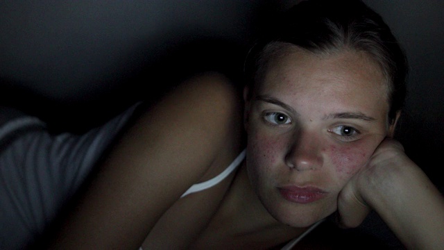 一个十几岁的女孩穿着睡衣躺在床上看电影视频素材