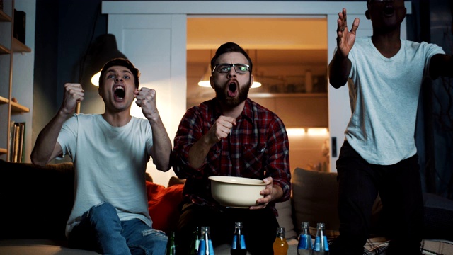 兴高采烈的多民族年轻男性球迷在家里一边吃着零食一边喊着看足球比赛。视频素材