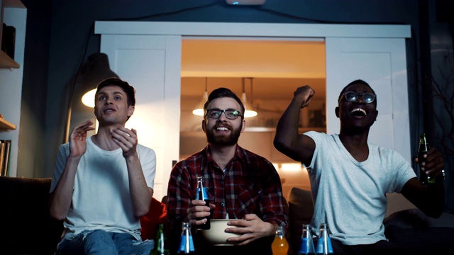 年轻快乐情绪多样的男朋友们一起看体育比赛，在家里用饮料庆祝胜利的慢动作。视频素材