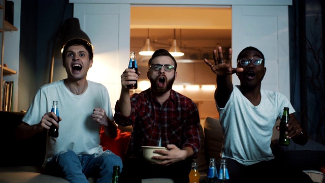 年轻快乐的多民族男性朋友们一起在家里喝着饮料喊着看体育篮球比赛的慢动作。视频素材