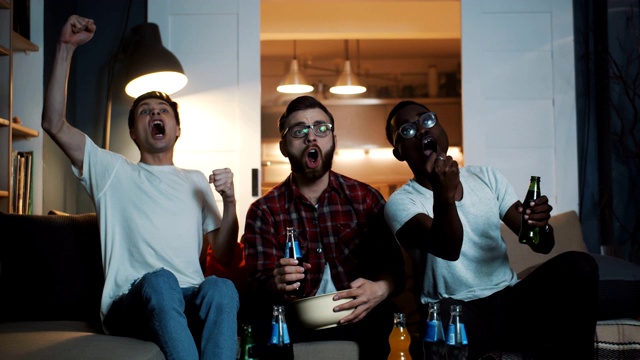 快乐的多民族男性体育爱好者欢呼，庆祝赢了一起在家里看比赛与饮料慢动作。视频素材