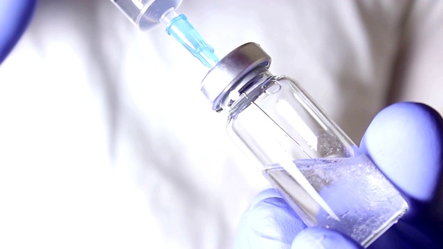 医生用注射器将溶液注射到疫苗小瓶中，混合药物，为注射病人做准备。视频素材