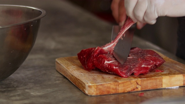 男子在木砧板上切生牛肉片，特写。烹调肉类视频素材