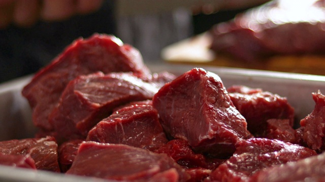 烹饪前，厨房里的红色生牛肉块。厨师在模糊的背景上切肉视频下载