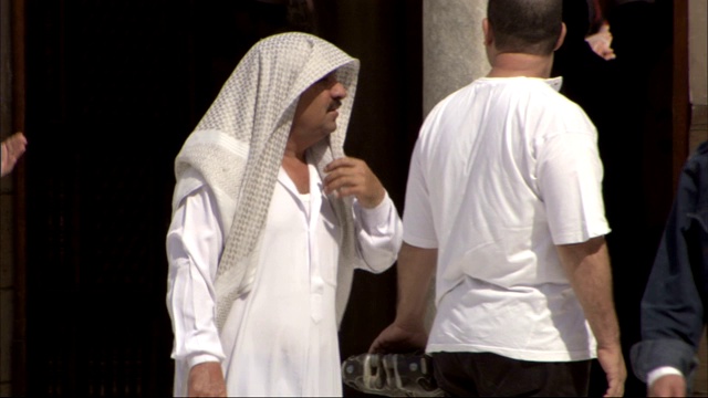 一名身穿传统服装的穆斯林男子在穿过清真寺的庭院时正整理着他的头巾。视频下载