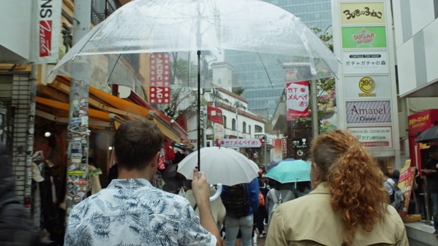 白种人男人和女人在雨伞下穿过东京视频素材