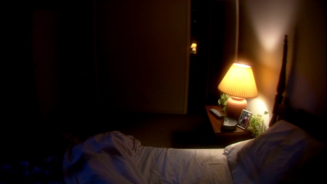 一个男人走进他的卧室，坐在他的床上，设置了闹钟。视频下载