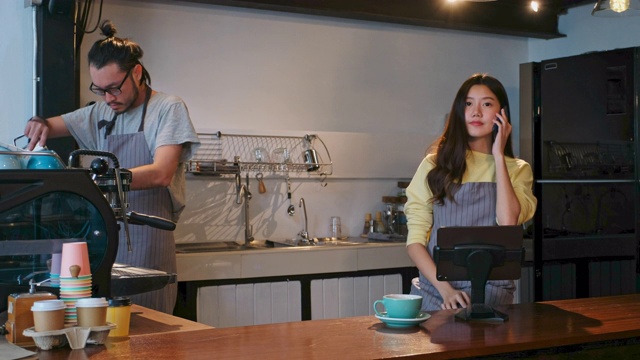 年轻的亚洲女性咖啡师，女招待，小企业主在咖啡馆咖啡馆背景的柜台通过数字平板电脑打电话点菜视频素材