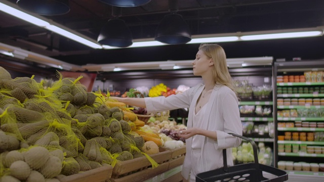 在超市:美丽的年轻女子走过新鲜农产品区，选择蔬菜并把它们放在她的购物车里。视频素材