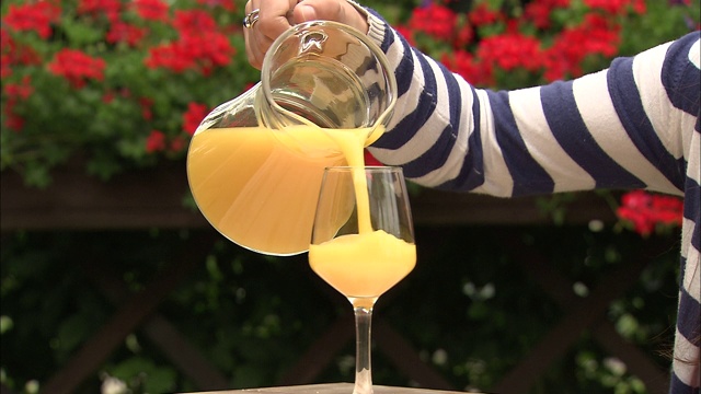 一只手举起一罐橙汁，把它倒进杯子里，再把它放在桌子上。视频素材
