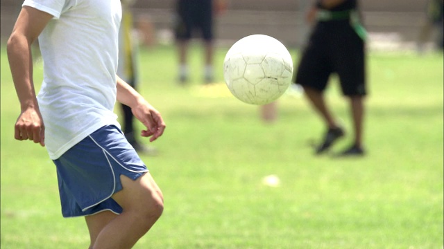 一个年轻人用他的脚、膝盖和头部在足球场上保持一个足球在空中。视频素材