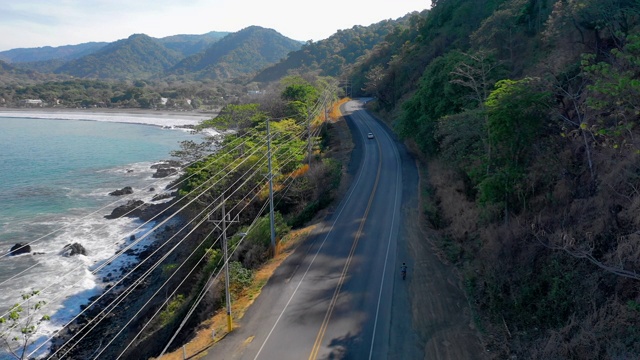 航拍:一名男子骑着自行车在悬崖边的山脚和附近的海洋-哥斯达黎加视频下载