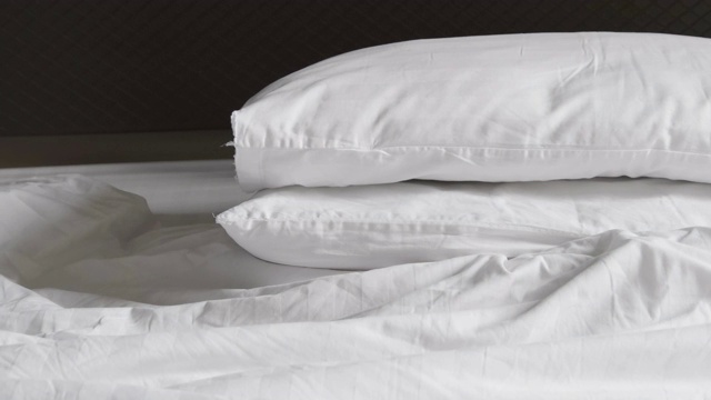 两个枕头乱成一团，白色的毯子凌乱不堪，早上醒来后发现床上有羽绒被。视频素材