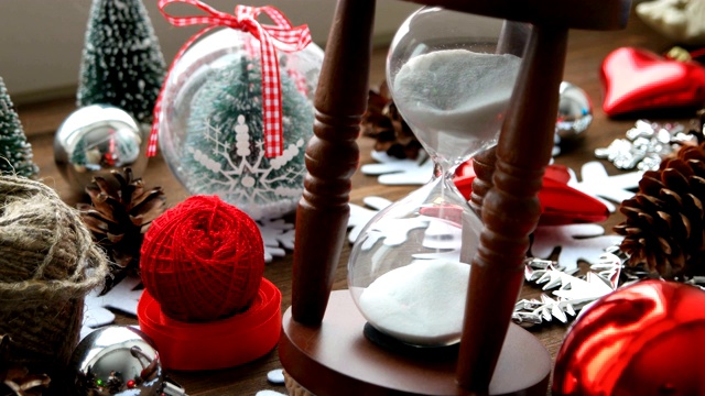 圣诞和新年的背景与礼物，丝带，球和不同的绿色装饰在木制的背景。木制沙漏计量着假期前的时间。视频素材