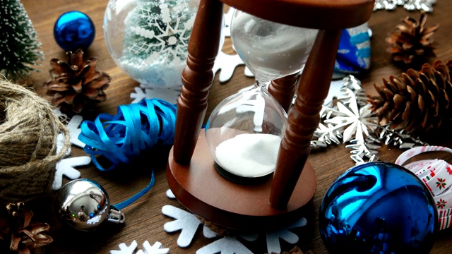 圣诞和新年的背景与礼物，丝带，球和不同的绿色装饰在木制的背景。木制沙漏计量着假期前的时间。视频素材