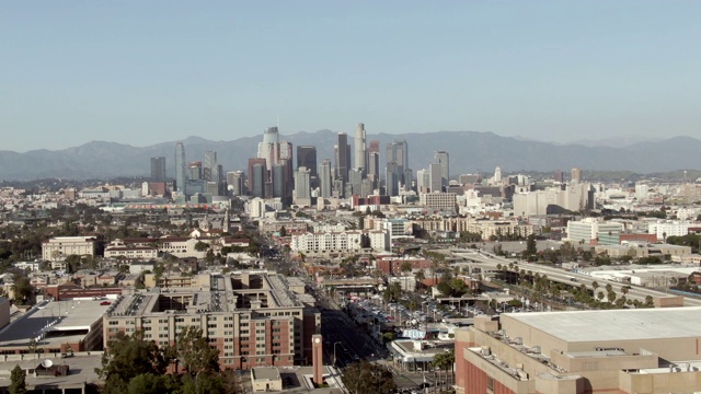 航拍:在阳光明媚的日子里，无人机在街道上的车辆对着晴朗的天空，在市中心的高楼大厦对着群山——加州洛杉矶视频素材