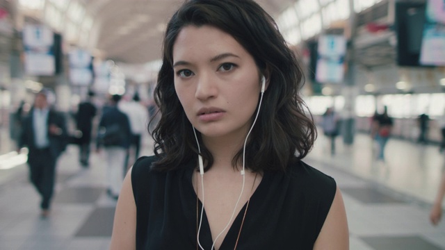 日本东京，一名女性戴着耳机站在繁忙的火车站里视频素材