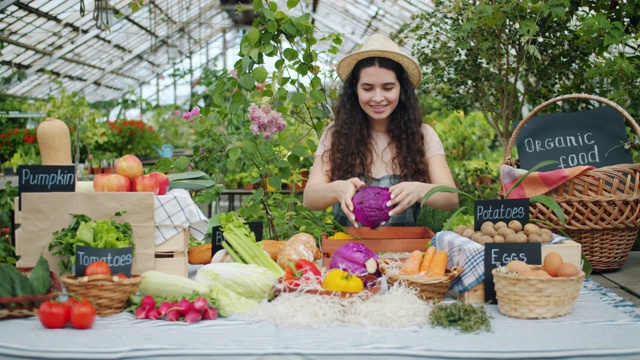 穿着围裙的快乐女农民微笑着把有机食品放在市场的桌子上视频下载