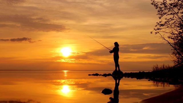 女人钓鱼在钓鱼杆旋转在夕阳的背景。视频素材