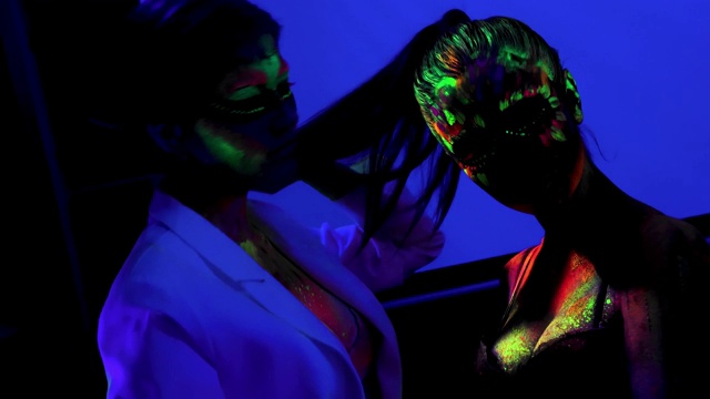 两个女孩用荧光彩妆，在紫外线下身体艺术设计，涂上五颜六色的脸视频素材