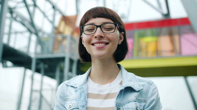 一个戴眼镜的漂亮女孩的肖像，微笑着看相机在户外视频素材