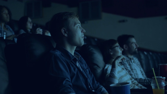 一群年轻人在电影院看电影，吃着爆米花，面带微笑视频素材