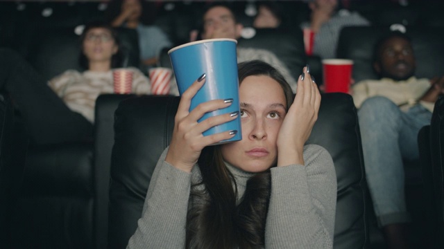 受惊吓的女人在电影院看恐怖电影，闭着眼睛吃爆米花视频下载