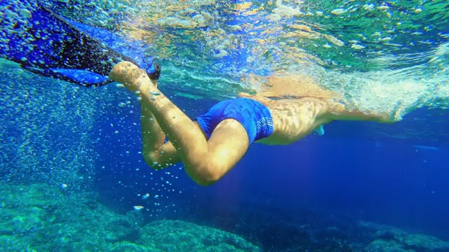 水下拍摄:阳光明媚的一天，男孩穿着脚蹼在海里游泳视频下载
