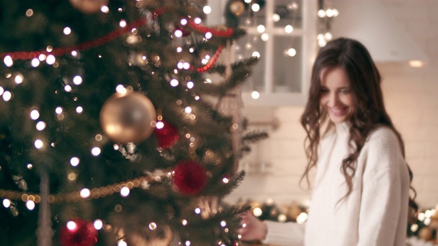 美丽的年轻女孩羡慕地看着家里的圣诞树。视频下载