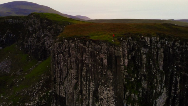在苏格兰斯凯岛海岸线的悬崖上，无人机拍摄到一个穿着荧光雨衣的人。视频下载