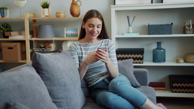漂亮女孩用现代智能手机触摸屏在沙发上笑视频素材