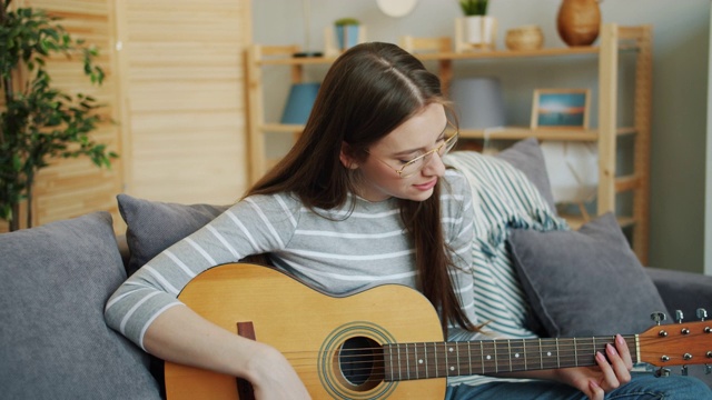 戴眼镜的年轻女子在家里弹吉他，享受音乐和闲暇时光视频素材