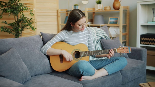 戴眼镜的美女坐在家里的沙发上弹吉他，摆出莲花的姿势视频素材