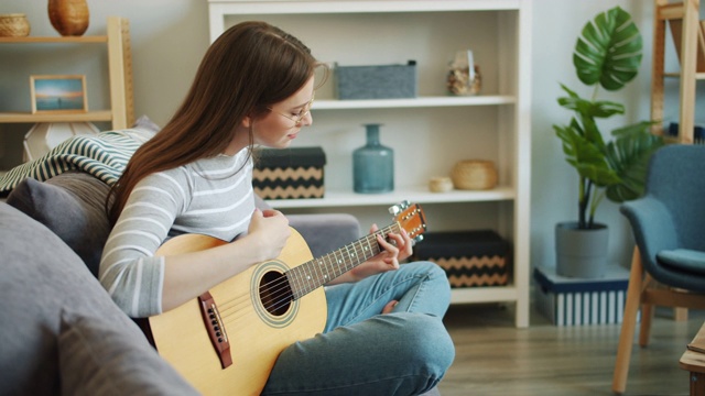 迷人的女孩独自在公寓里弹吉他享受音乐的慢镜头视频素材