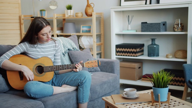漂亮的年轻女子在舒适的公寓里弹吉他，独自玩乐视频素材