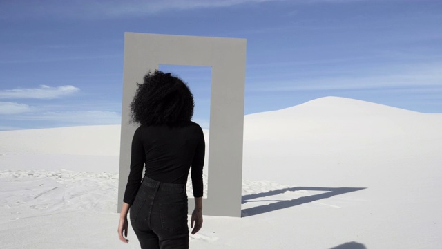 一个穿着黑衣的女人穿过沙漠中的门框，很宽视频素材