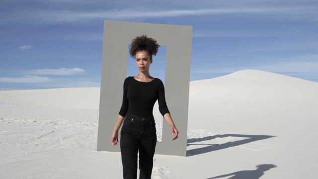 在沙漠中，一个穿着黑衣的女人走过门框视频素材