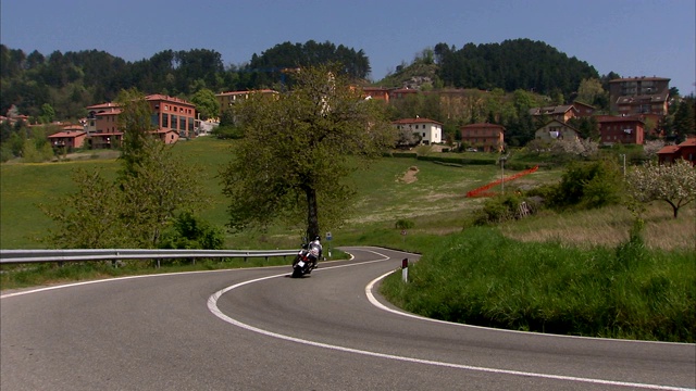 摩托车手在山坡下的乡间小路上骑摩托车。视频素材