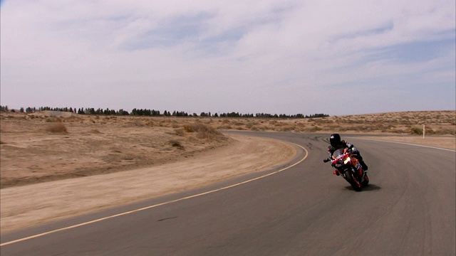 摩托车在弯弯曲曲的沙漠公路上飞驰。视频素材