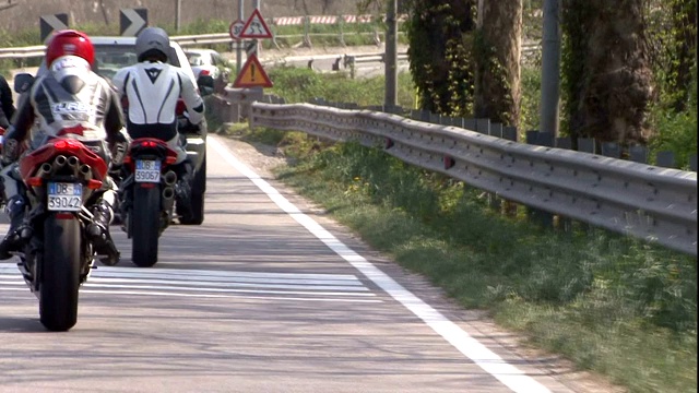 一群摩托车手在一条狭窄的道路上跟着一辆汽车。视频素材