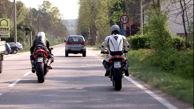 在一条繁忙的乡村道路上，两个摩托车手跟在一辆汽车后面。视频素材